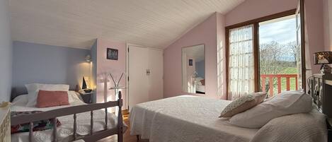 A bedroom with a wooden bed, a bench, a desk, and a window with a view of trees.