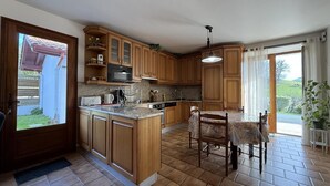 A kitchen with wooden cabinets, a central island, and a dining area with chairs. - Aguerrea - Macaye - Gîte (MACAYE)