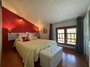 Un dormitorio con cama, mesita de noche, lámpara, ventana con cortinas y puerta.