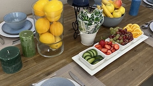 A dining table set with plates, bowls, and a variety of fruits and vegetables.