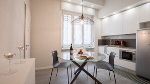 Une cuisine moderne avec des meubles blancs, une table à manger en verre et un luminaire suspendu.