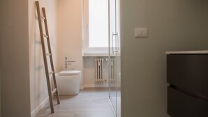 Un couloir étroit avec des toilettes, un radiateur et une fenêtre.