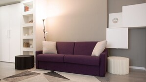 Un salon moderne avec un canapé violet, une étagère blanche et un tapis à motifs géométriques.
