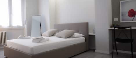 A bedroom with a bed, bedside table, chair, and a large mirror.