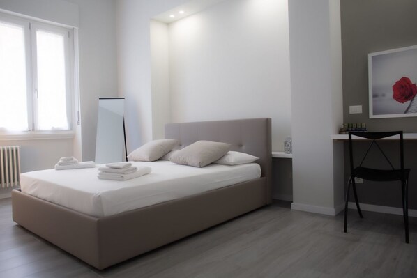 A bedroom with a bed, bedside table, chair, and a large mirror.