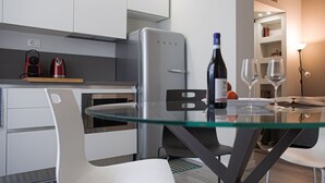 Une cuisine moderne dotée d’un four encastré, d’un réfrigérateur en acier inoxydable et d’une table à manger en verre, accompagnée de deux chaises blanches.