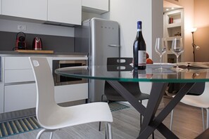A modern kitchen with a built-in oven, a stainless steel refrigerator, and a glass dining table with two white chairs. - AQUILEIA, 10 - Bilocale a due passi dai Navigli e Museo Scienza (Milano)