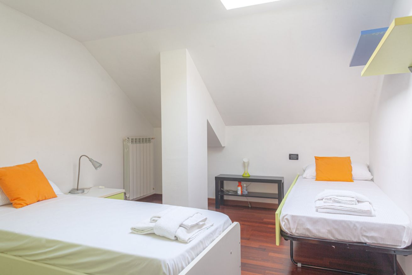 A room with two beds, a radiator, a table with a lamp, and a shelf with toiletries.