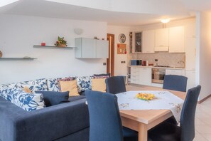 A modern living room with a sofa, chairs, a dining table, and a kitchen area with cabinets and appliances.