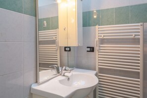 Une salle de bain équipée d’un lavabo, d’un miroir, de porte-serviettes et d’un luminaire fixé au mur.