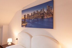 Une chambre d’hôtel avec un tableau représentant un paysage urbain, un lit et une table de chevet avec une lampe.