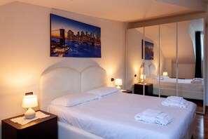 A hotel room with a large bed, a nightstand with a lamp, a mirror, and a cityscape painting on the wall. - ASIAGO, 41 · Quartiere Gorla, verde in città (Milano)