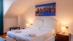 Une chambre d’hôtel avec un grand lit, deux tables de chevet, un tableau représentant un paysage urbain accroché au mur et une vue sur la ville.