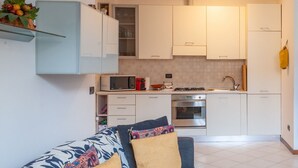 A modern kitchen with white cabinets, a microwave, stove, and oven. There is a small dining area with a table and chairs. - ASIAGO, 41 · Quartiere Gorla, verde in città (Milano)