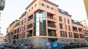 Un immeuble à plusieurs étages doté de balcons, un fourgon bleu garé devant, et une personne qui marche sur le trottoir.