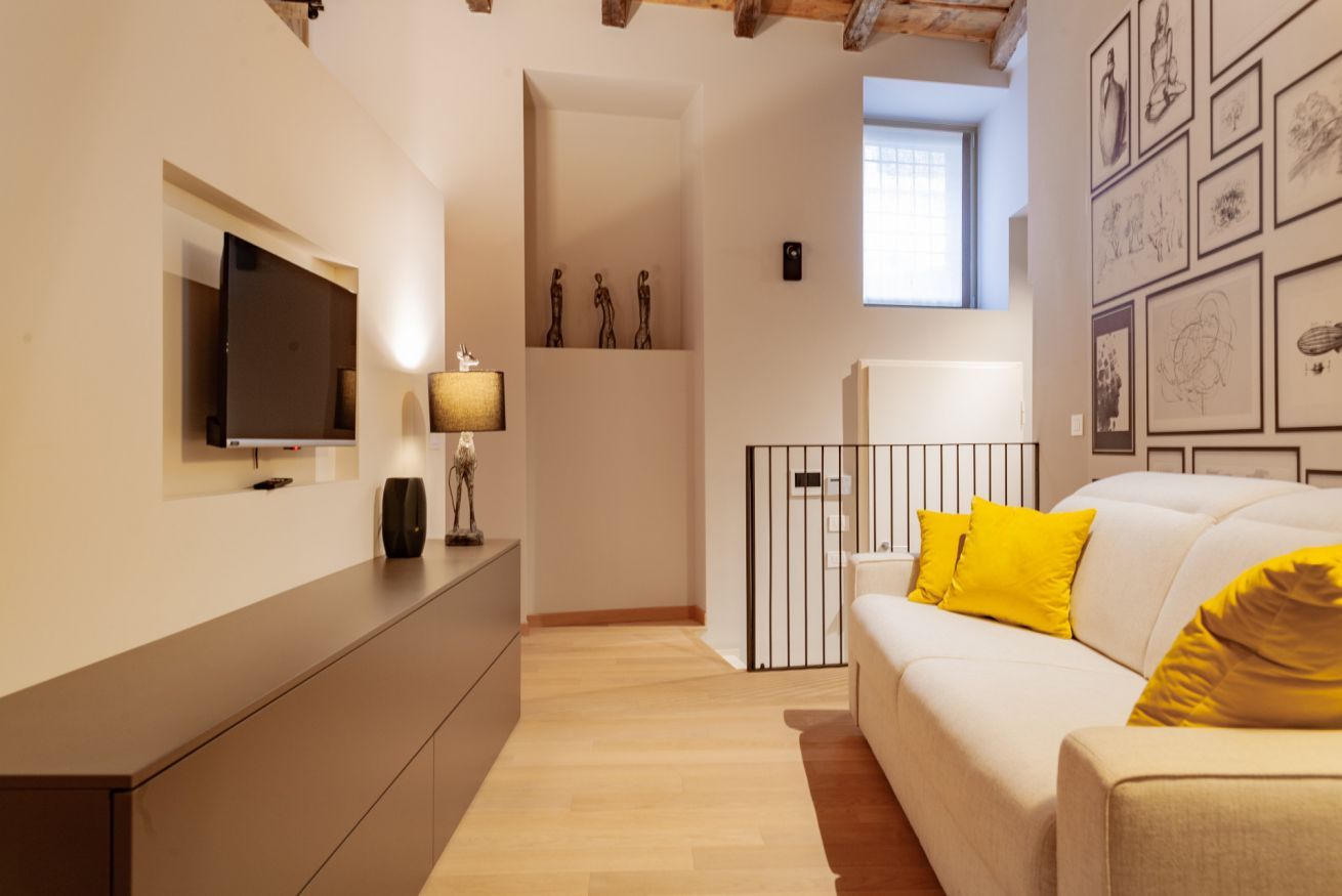 Un salon moderne avec un téléviseur à écran plat, un canapé avec des coussins jaunes, une lampe et des œuvres d’art accrochées aux murs.