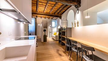 A modern kitchen with a wooden ceiling, white cabinetry, and a dining area with chairs and a table.