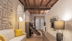 A modern living space with a staircase, a sofa with yellow cushions, a lamp, and framed artwork on the walls. - VIA SIMONE MAYR, 2 · Bergamo città Alta - appartamento di charme (Bergamo)