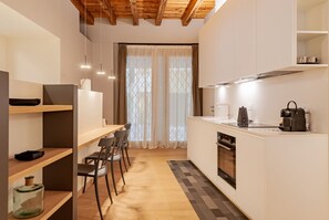 A compact kitchen with a dining area, wooden ceiling, and a view through a window with curtains. - VIA SIMONE MAYR, 2 · Bergamo città Alta - appartamento di charme (Bergamo)