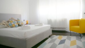 A hotel room with a bed, a yellow chair, and a geometric patterned rug.