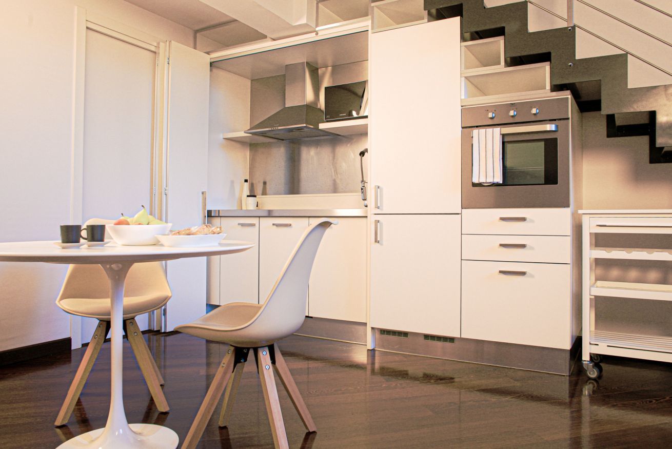 Une cuisine moderne avec des meubles blancs, un four en acier inoxydable et un coin repas comprenant une table et des chaises.