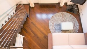 A modern interior with a wooden floor, a round patterned rug, a white sofa, and a metal railing.