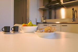 A kitchen with a white countertop, a bowl of fruit, a cup, and a plate of food.