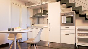 A modern kitchen with white cabinetry, a stainless steel oven, and a dining area with a table and chairs.