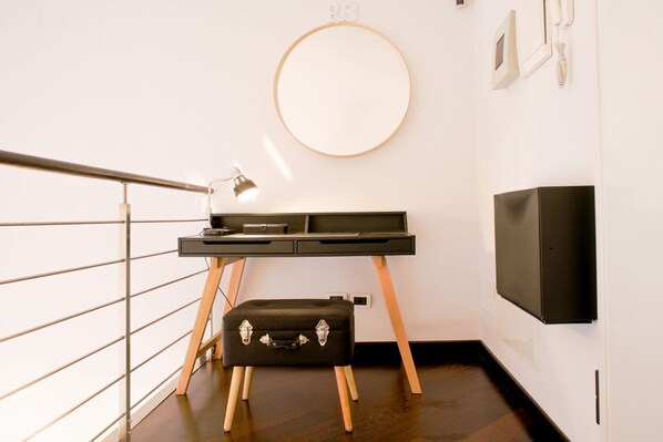 Une chambre moderne équipée d’un bureau, d’un miroir rond, d’une télévision et d’un petit pouf noir.
