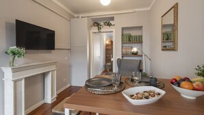 A dining area with a wooden table, a flat-screen TV mounted on the wall, a fireplace, and a mirror. - Buenos Aires 49 – Lungo la via dello shopping (Milano)