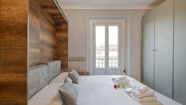 A hotel room with a wooden accent wall, a bed with pillows, a radiator, a window with a view, and a wardrobe. - Buenos Aires 49 – Lungo la via dello shopping (Milano)