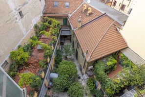 A courtyard with potted plants, a small garden area, and a building with a tiled roof. - Buenos Aires 49 – Lungo la via dello shopping (Milano)