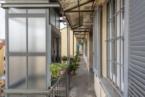 A narrow corridor with a metal railing, potted plants, and a series of windows on one side.