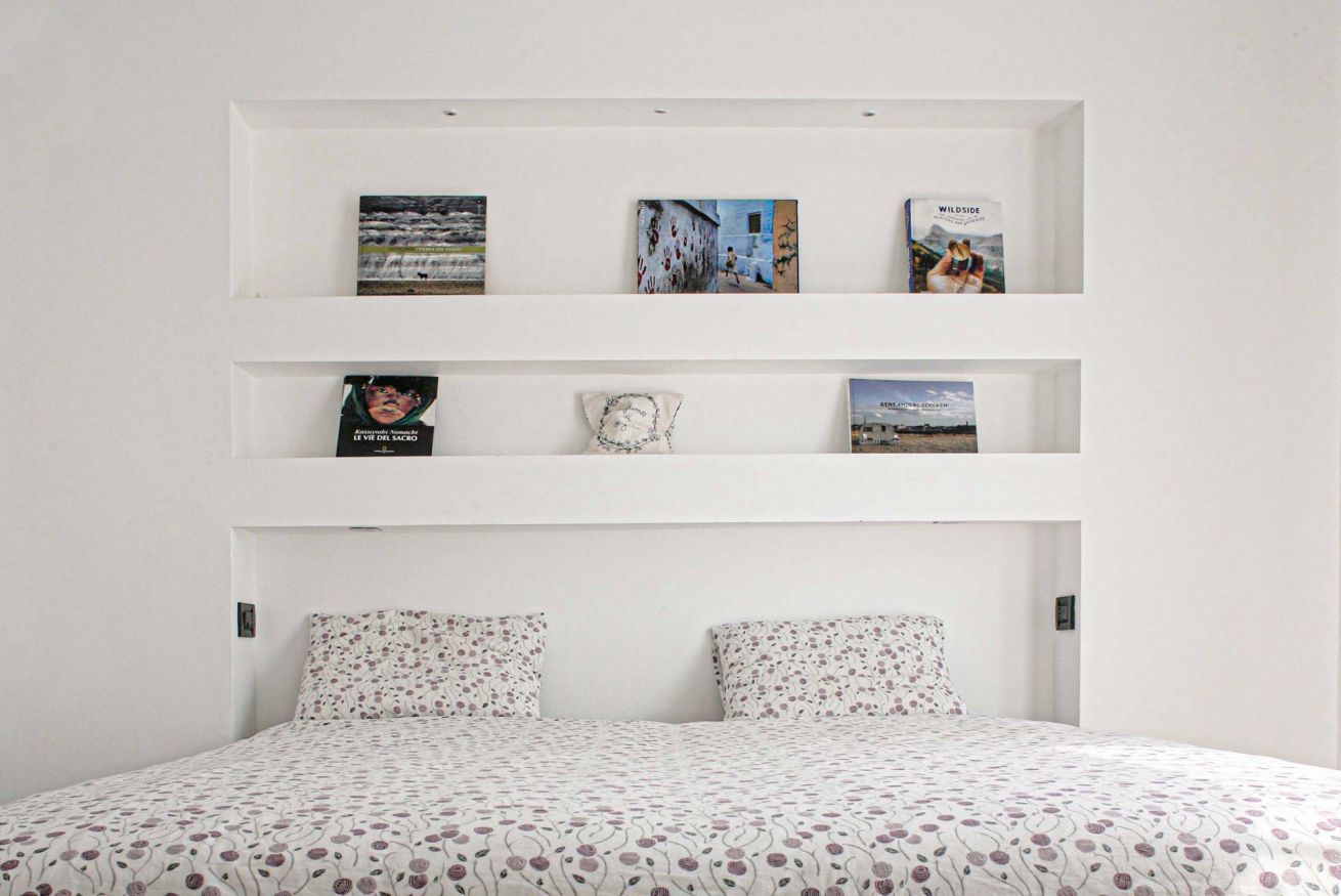 A bedroom with a bed, two pillows, and three shelves with books and a decorative item.
