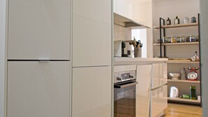 Una cocina con muebles blancos, horno empotrado y estante con frascos y utensilios de cocina.