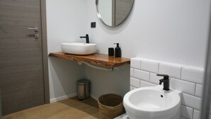 Un baño con tocador de madera, dos lavamanos, un espejo y un cubo de basura.