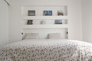 A bedroom with a bed, two pillows, a white wall, and three shelves with books and a clock. - BUENOS AIRES, 51 - Moderno appartamento di design nel cuore di Milano (Milano)
