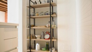 Une cuisine avec un meuble en bois servant d’étagère, où sont rangés des bocaux, une bouilloire et des ustensiles de cuisine.