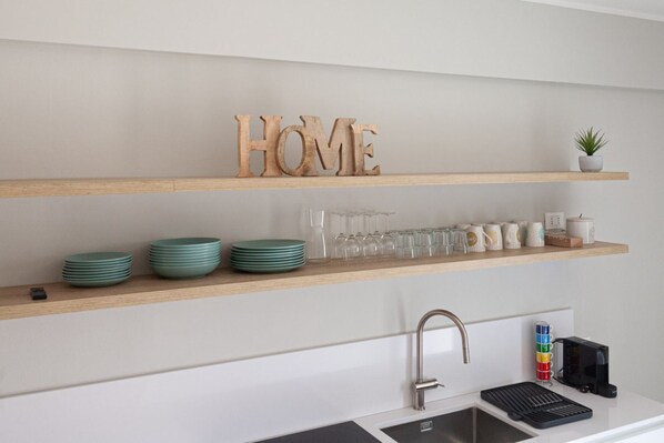 A kitchen with wooden shelves, a sink, and a coffee machine.