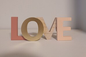 Drei Holzbuchstaben, die ‚LOVE‘ buchstabieren, mit einem runden Ring zwischen dem ‚O‘ und ‚V‘ auf einer schlichten Fläche.