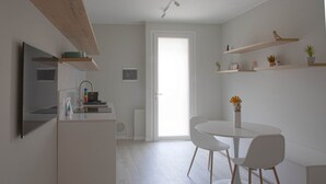 A modern kitchen with white cabinetry, a dining area with a round table and white chairs, and built-in shelving with plants. - CASATI, 2 · Glamour in città tra shopping e vita notturna (Milano)