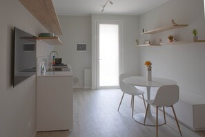 A modern kitchen with white cabinetry, a dining area with a round table and white chairs, and built-in shelving with plants. - CASATI, 2 · Glamour in città tra shopping e vita notturna (Milano)