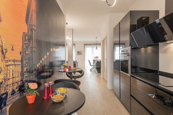 A modern kitchen with a large window, a dining area with a round table, and a mural of a cityscape on the wall.