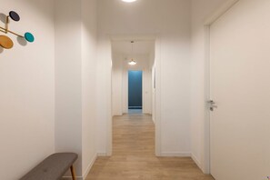 A narrow hallway with wooden flooring, white walls, and a bench on the left.