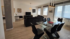 Ein modernes Wohnzimmer mit einem Glastisch, schwarzen Stühlen, einem schwarzen Sofa und einem Fernseher.