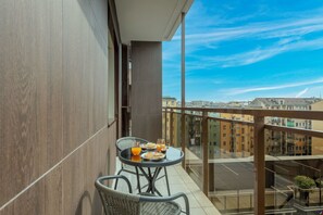 A balcony with a table set for breakfast, a chair, and a view of the cityscape.