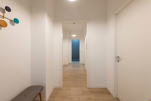 A narrow hallway with wooden flooring, white walls, and a bench on the left. - Via Foppa 7 – Ampio trilocale (Milano)
