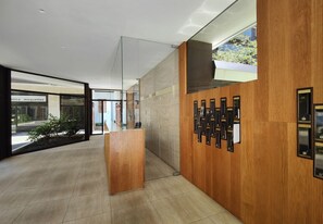 A modern reception area with a wooden reception desk, a glass partition, and a wall-mounted information board.