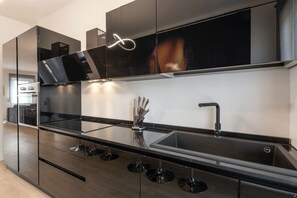 A modern kitchen with a black countertop, stainless steel appliances, and a large window above the sink.
