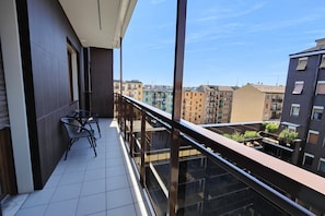 Un balcon doté d’une balustrade en verre, une petite table avec des chaises et une vue sur les bâtiments voisins.